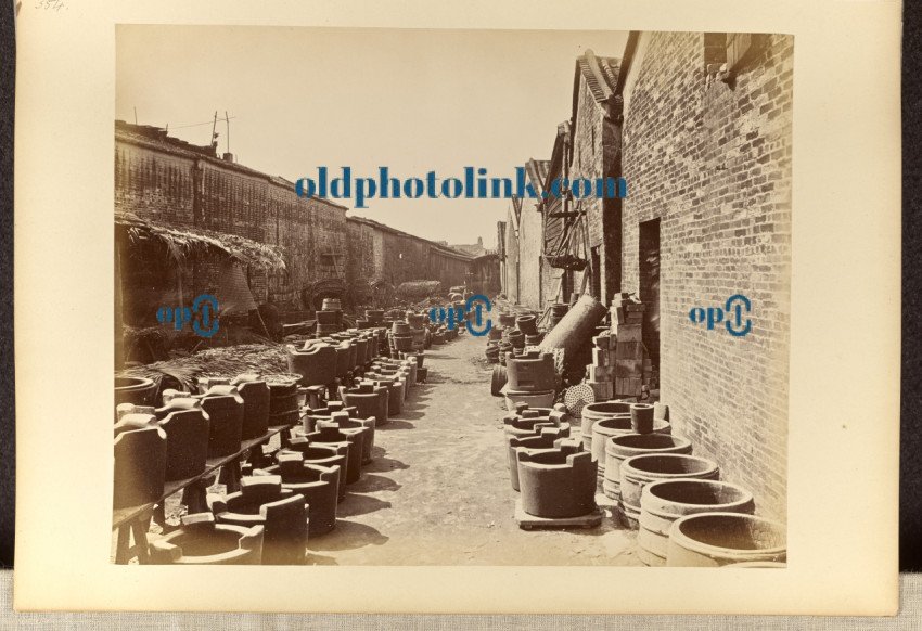 View of an alley bordered by brick buildings and containers on the ground 1870